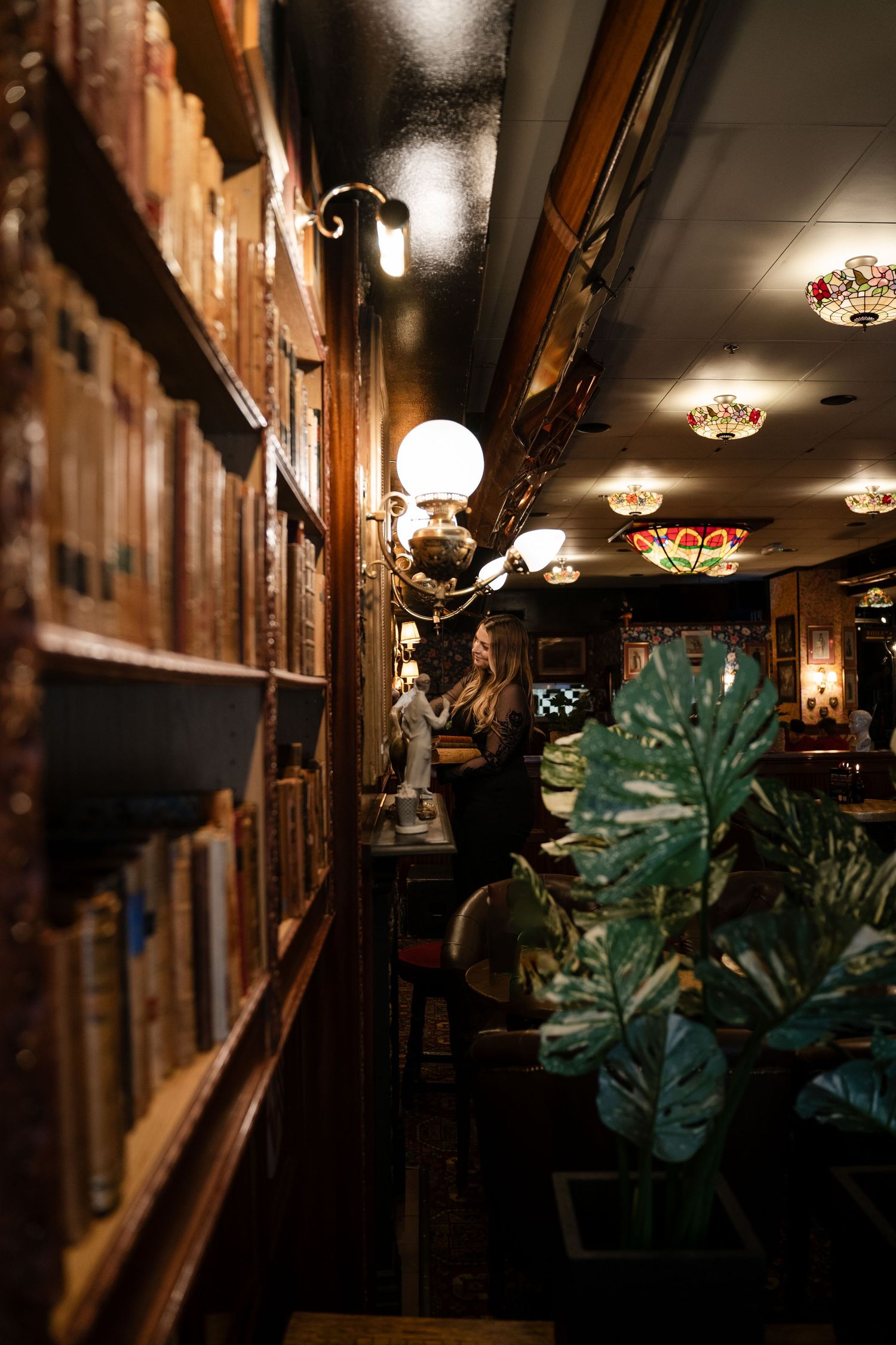 Moody interior of a vintage library bar with glowing globe lights and wooden bookshelves.