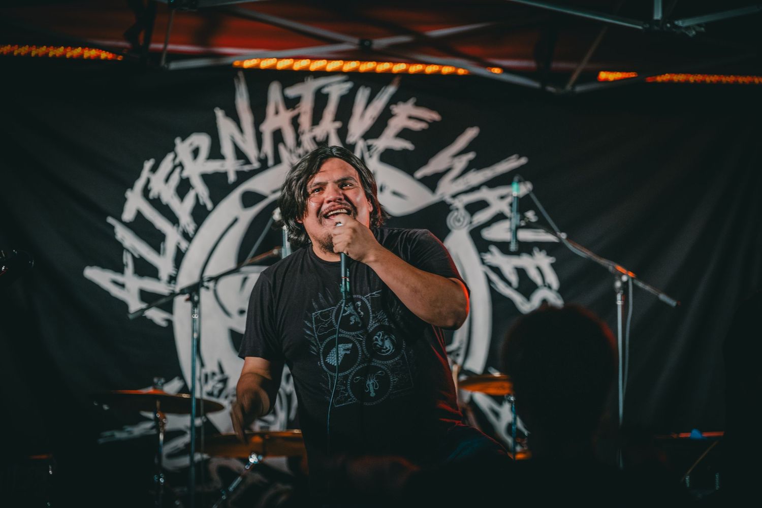 A performer singing on stage with 'Alternative Lives' banner visible in the background.