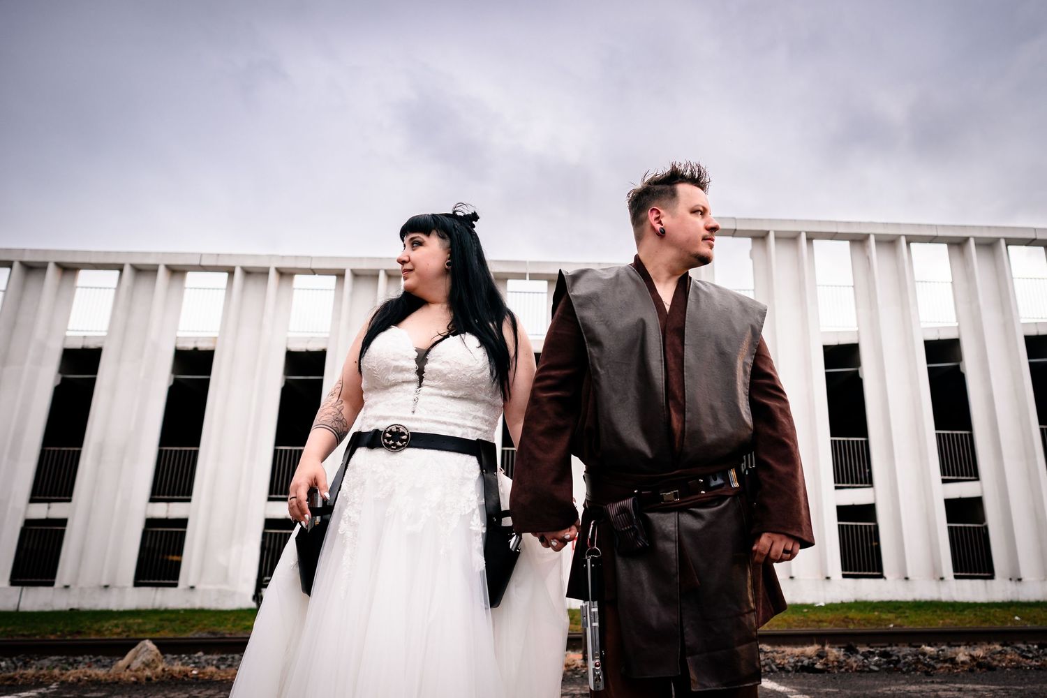 Wedding party members pose outdoors against a white architectural backdrop under cloudy skies.