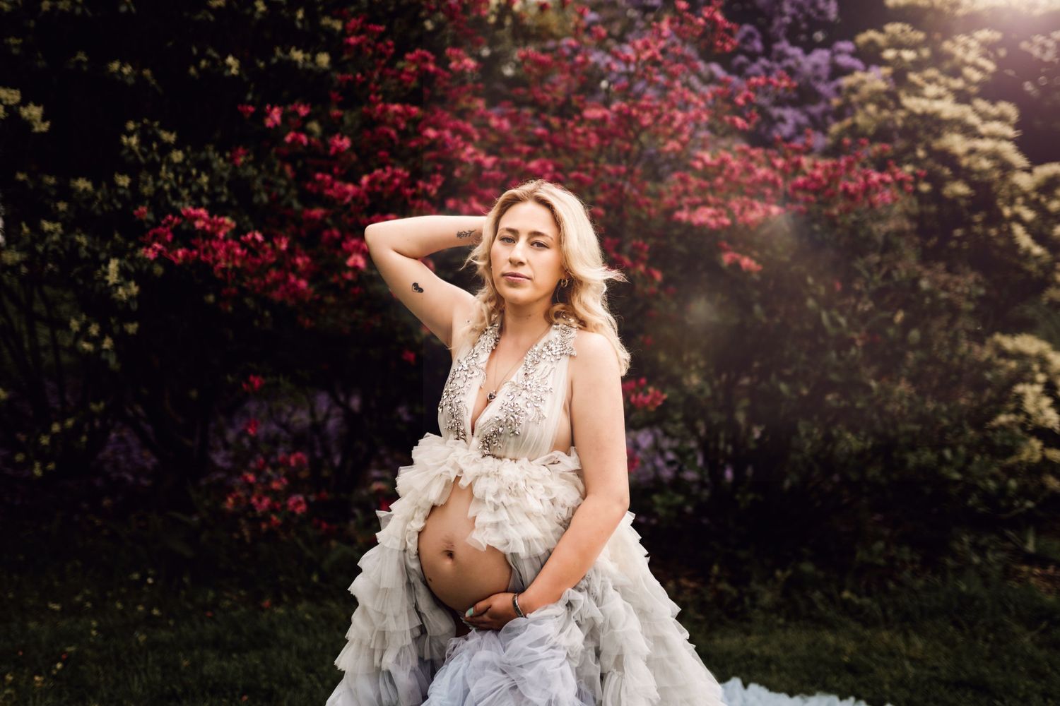 Ethereal maternity portrait in flowing ruffled dress against blooming garden backdrop.