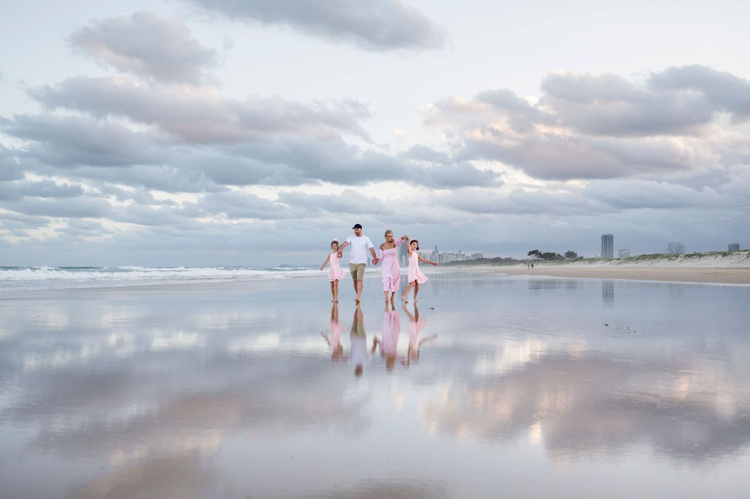 Family in white clothes walking on reflective beach at sunset.