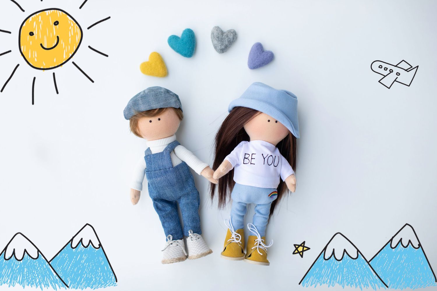 Two handmade fabric dolls holding hands with colorful felt hearts on a white background with doodles.