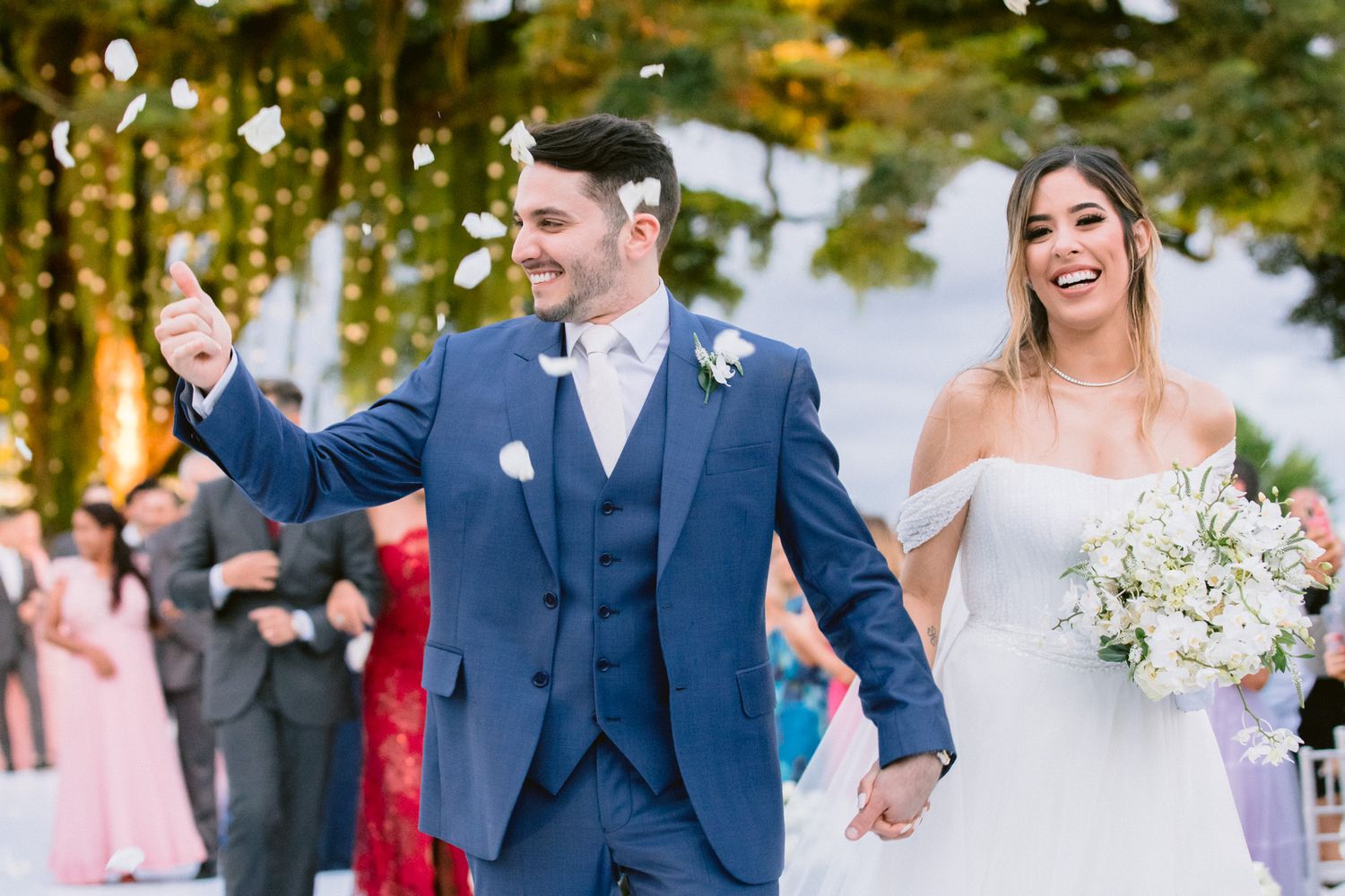 Joyful wedding celebration with confetti as newlyweds walk holding hands outdoors.