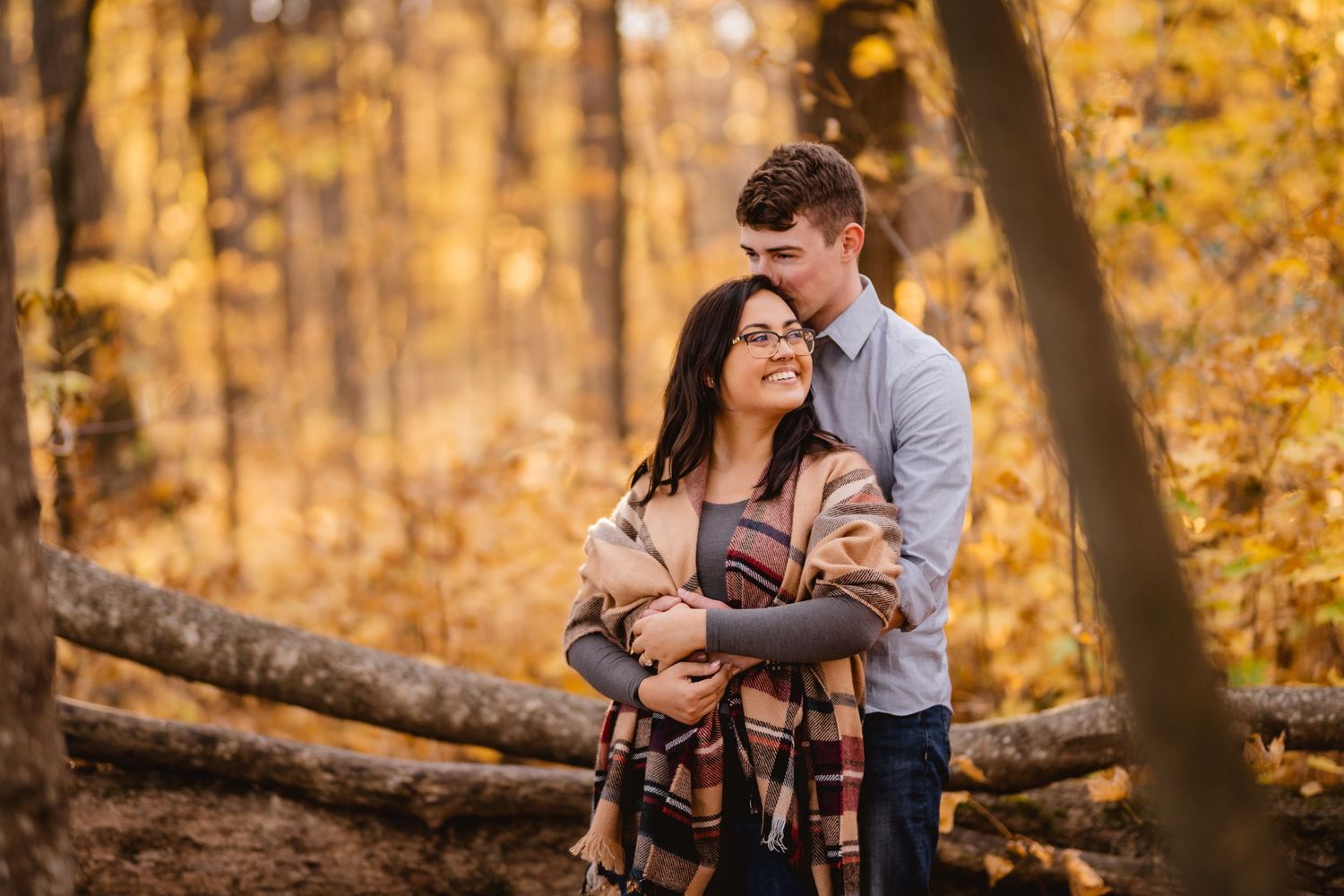 A man kisses his betrothed's head in front of a forest of golden trees
