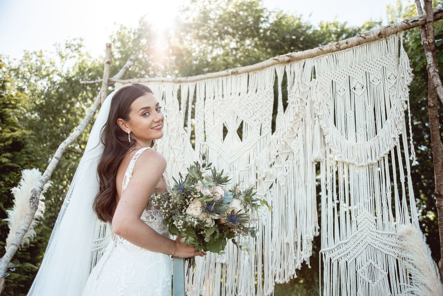 Bohemian wedding setup with macrame backdrop and natural lighting in an outdoor garden setting.