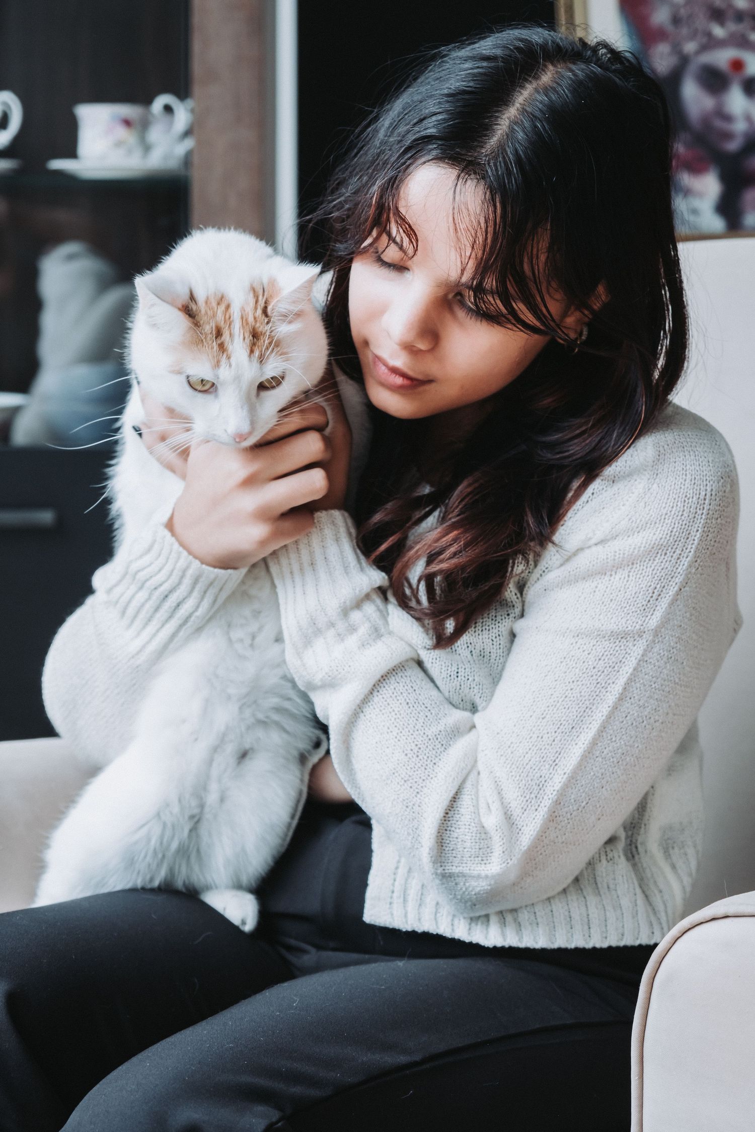 Person in white sweater cuddles with white cat while relaxing on couch.