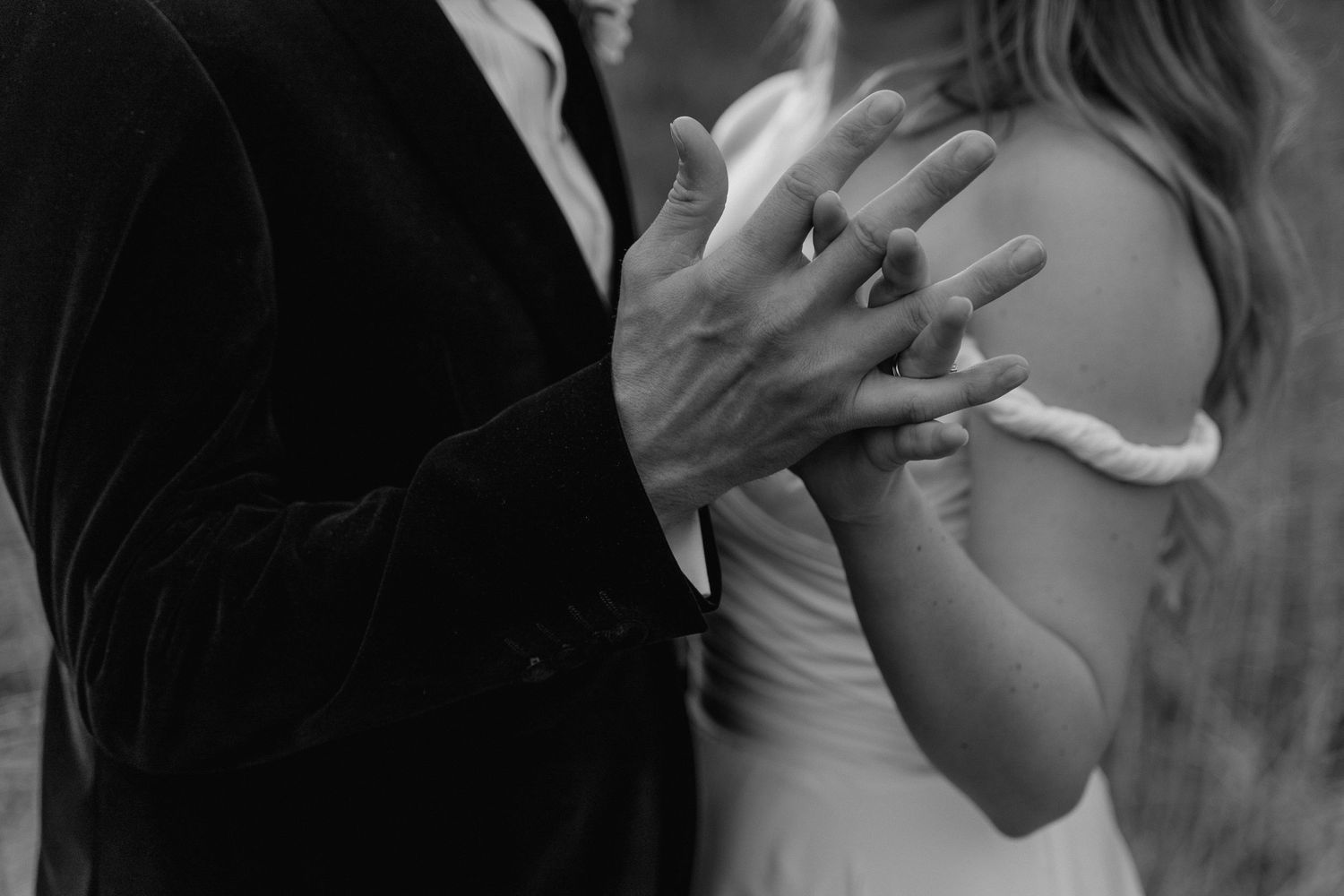 a black and white image of a bride and grooms hands, fingers entwined.