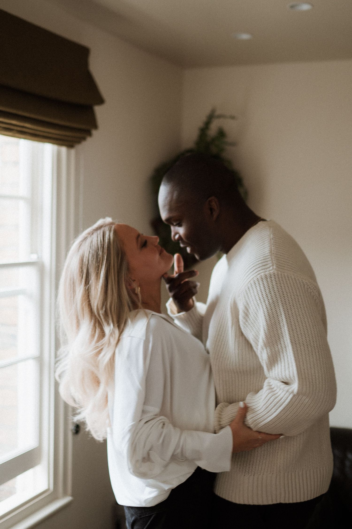 A tender moment shared between a couple in cozy white sweaters by a window.
