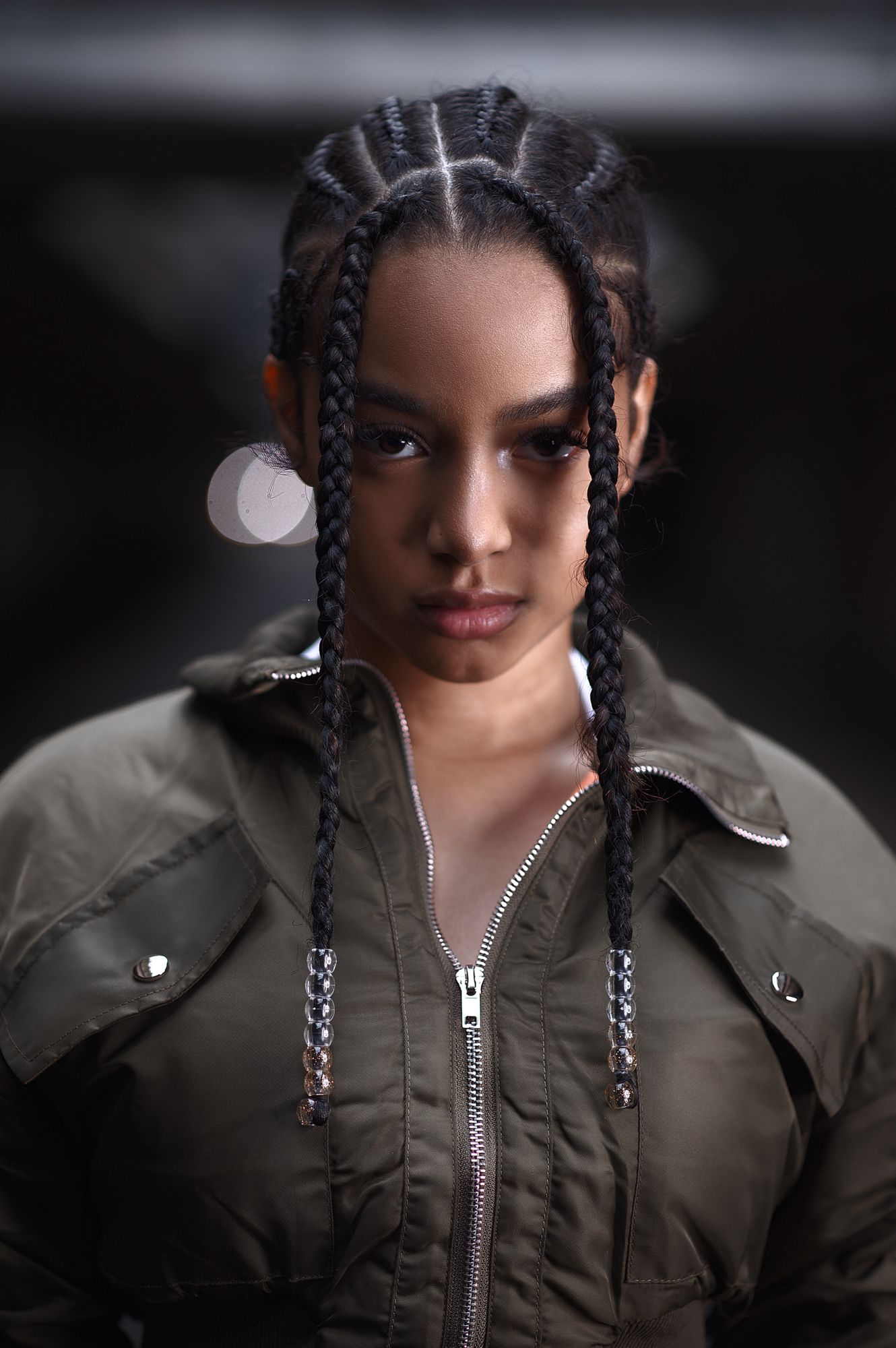 Urban portrait featuring braided hairstyle and olive bomber jacket in moody lighting.