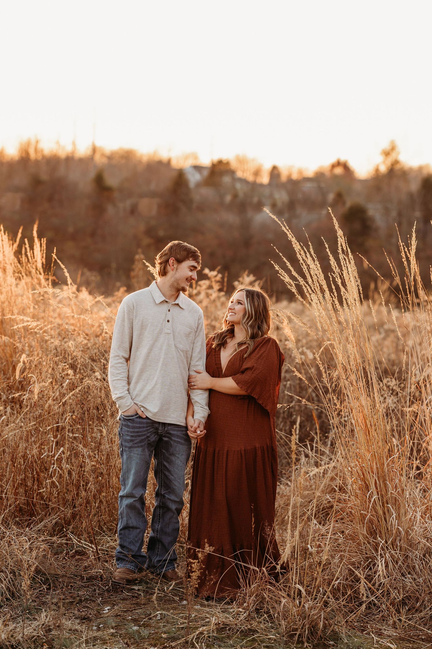 Couple standing in golden sunlit field during autumn engagement photoshoot.