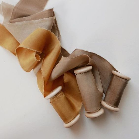 Collection of silk ribbons in neutral beige and caramel tones wrapped around wooden spools.