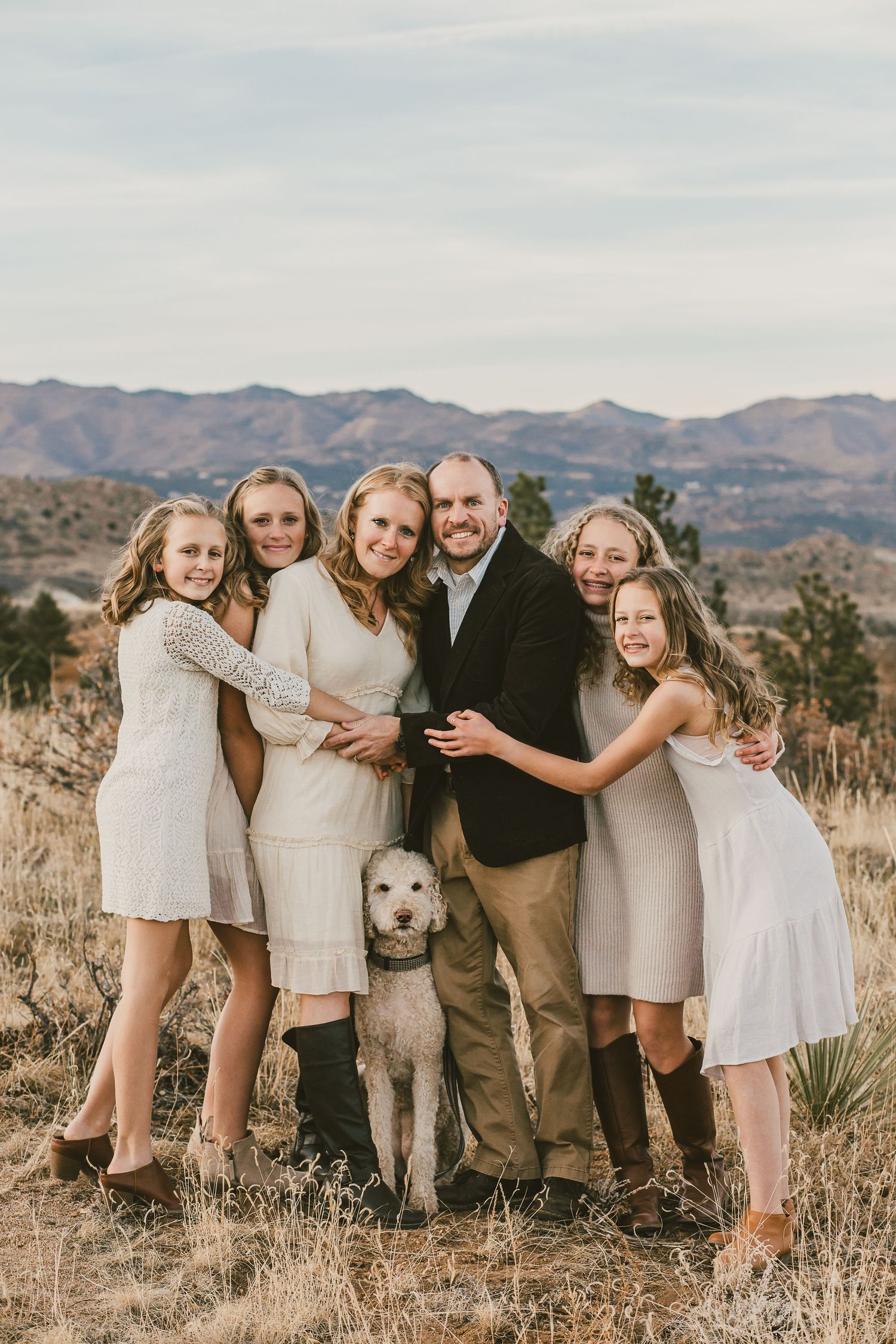Family portrait with white dog against mountain landscape backdrop.
