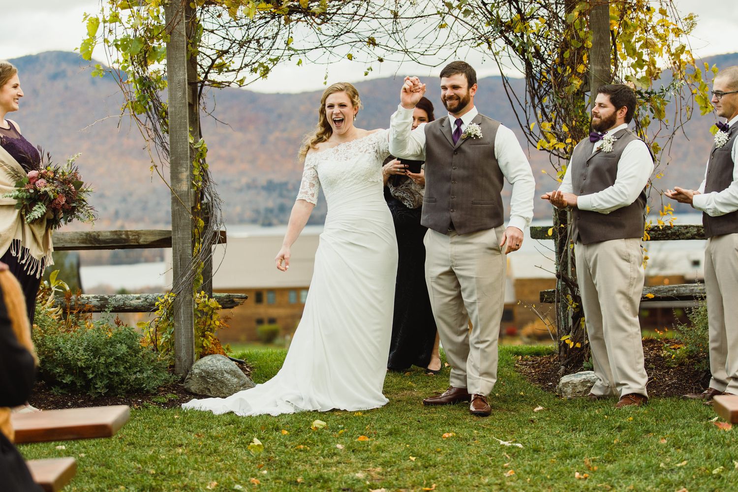 A wedding ceremony takes place outdoors with mountain views and fall foliage in the background.
