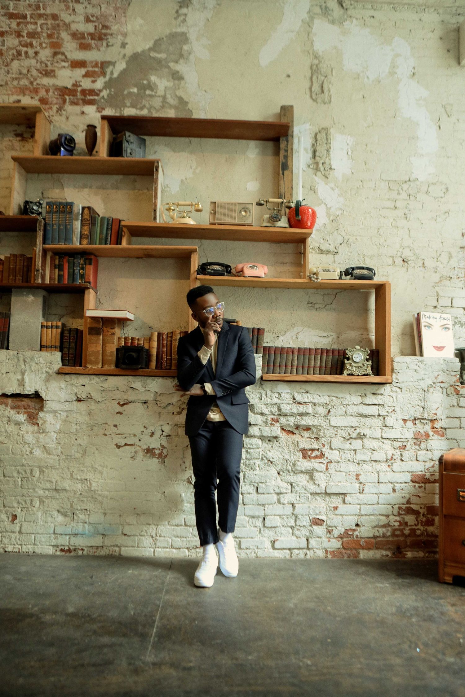 A casual portrait in front of wooden shelving and exposed brick wall interior.
