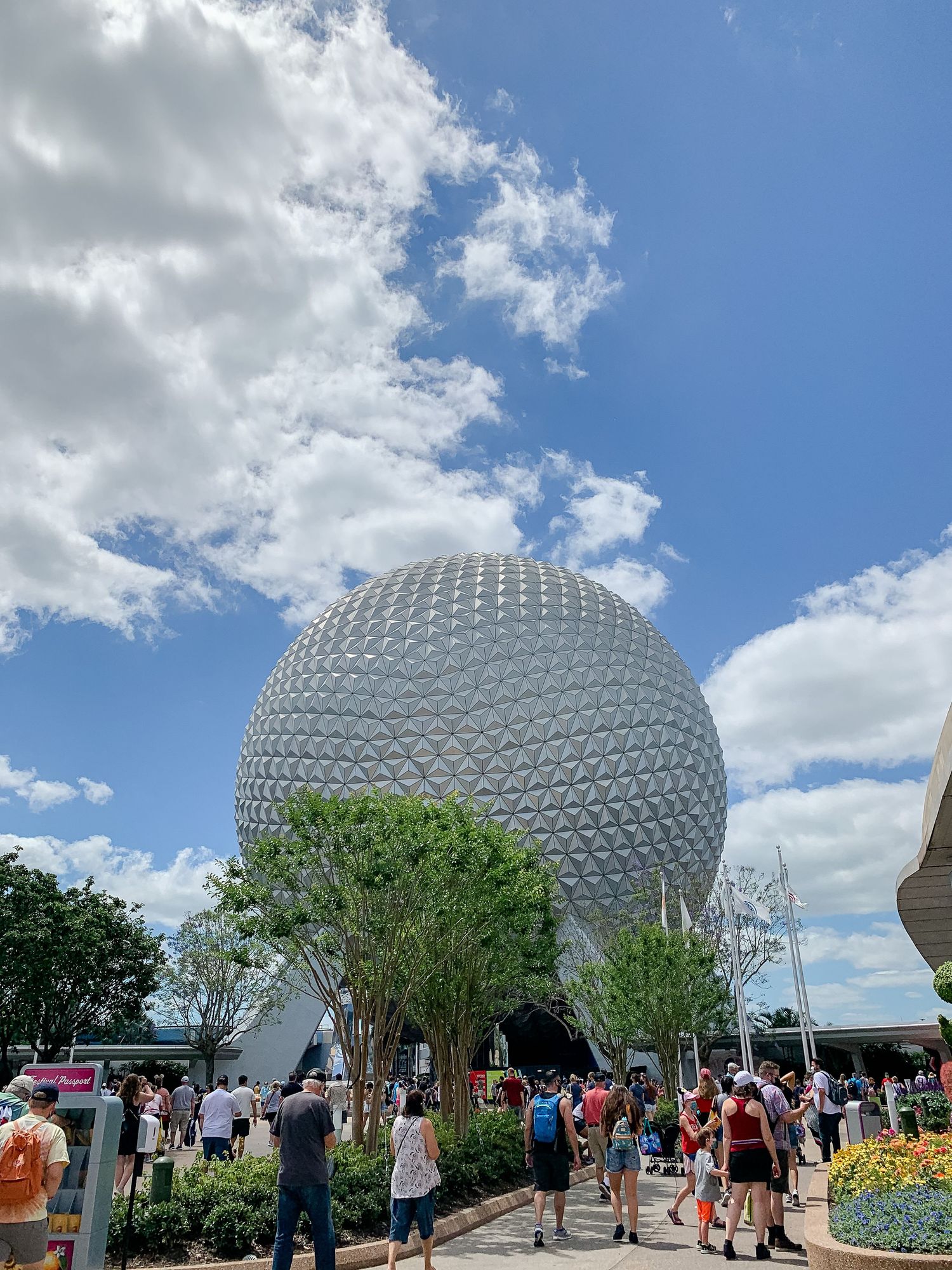 Spaceship Earth sphere at EPCOT under blue skies with crowds gathering outside.
