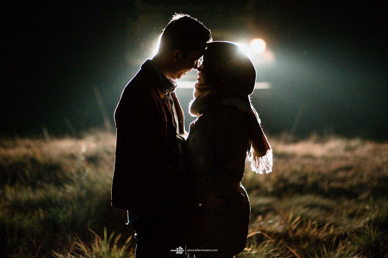 Backlit silhouette of couple embracing in a misty field at night.