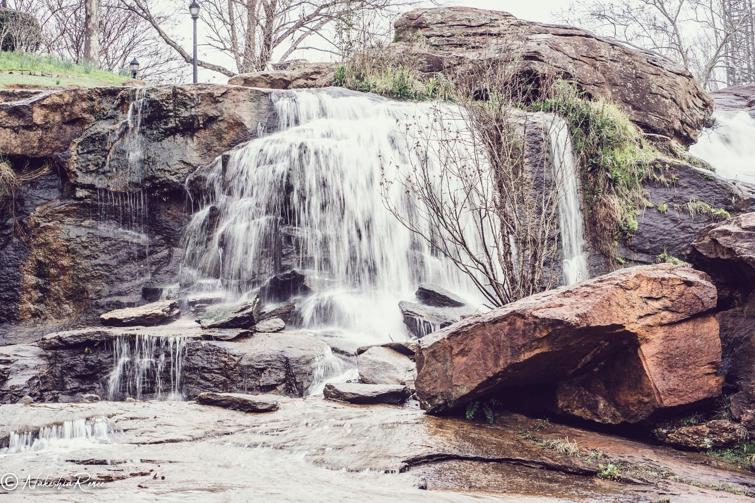 A cascading waterfall flows over rocky terrain with large boulders in a natural setting.
