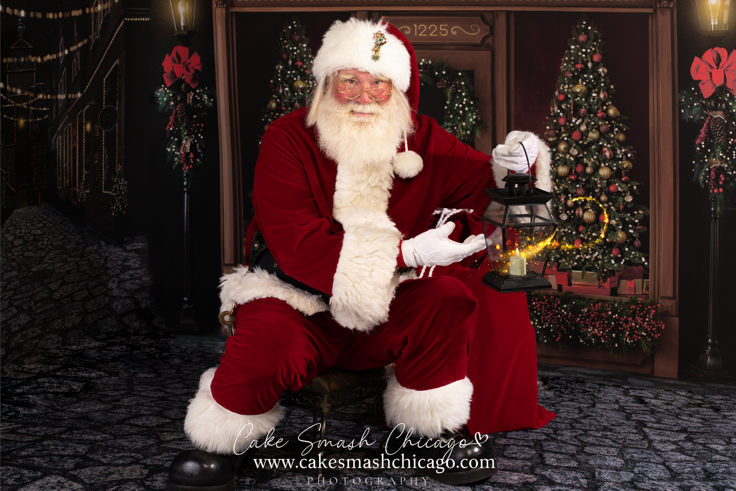 Traditional holiday figure in red suit seated in front of decorated trees and wreaths in studio setting.
