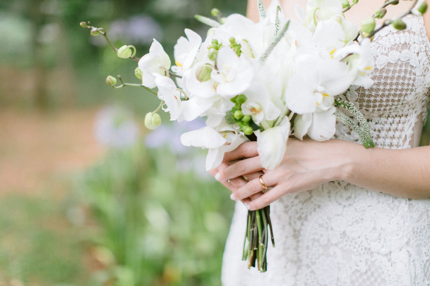 Delicate white floral bouquet with lilies and greenery held by bride in lace dress.