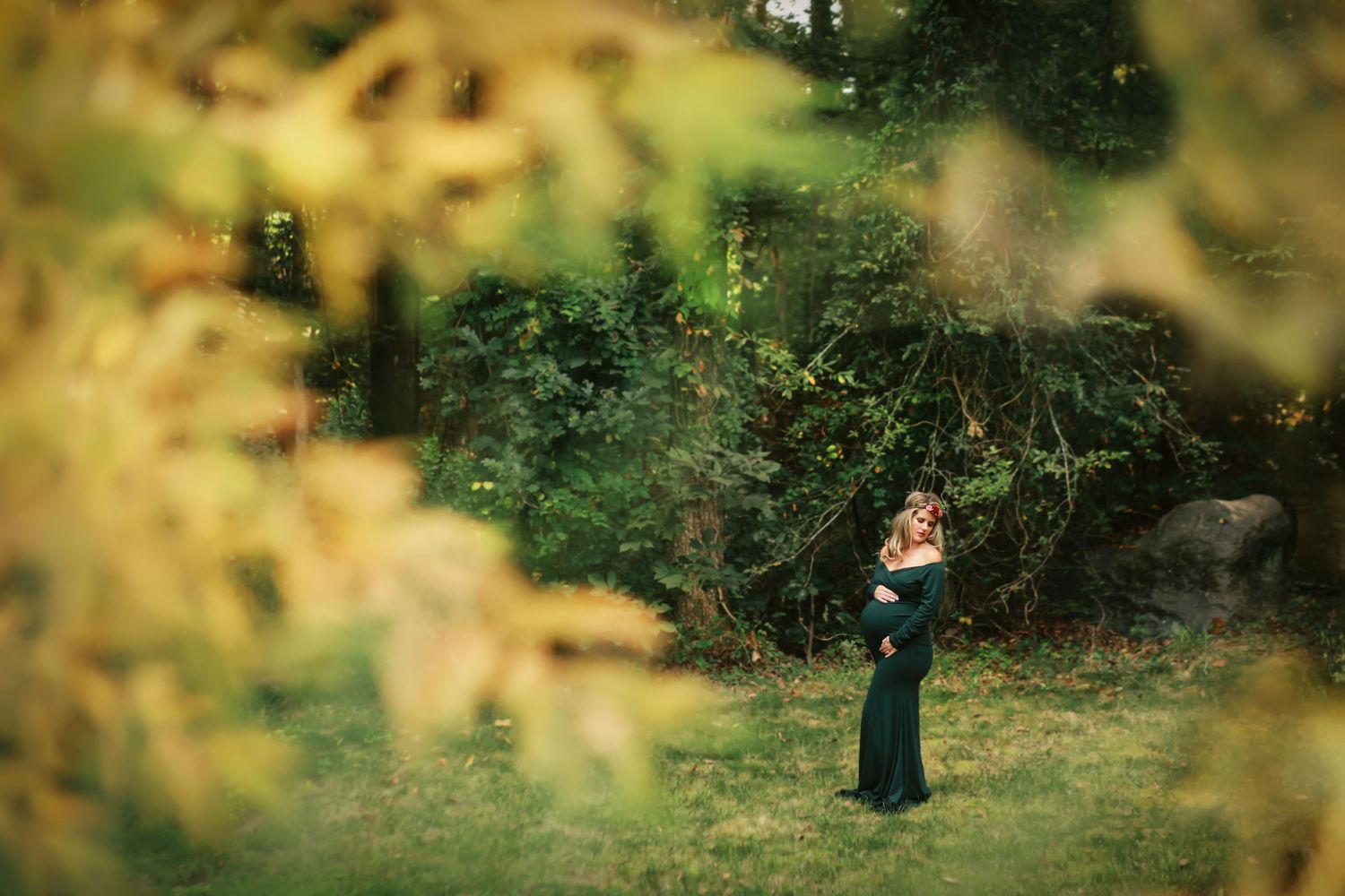Maternity photo of a woman in a dark dress framed by autumn foliage.