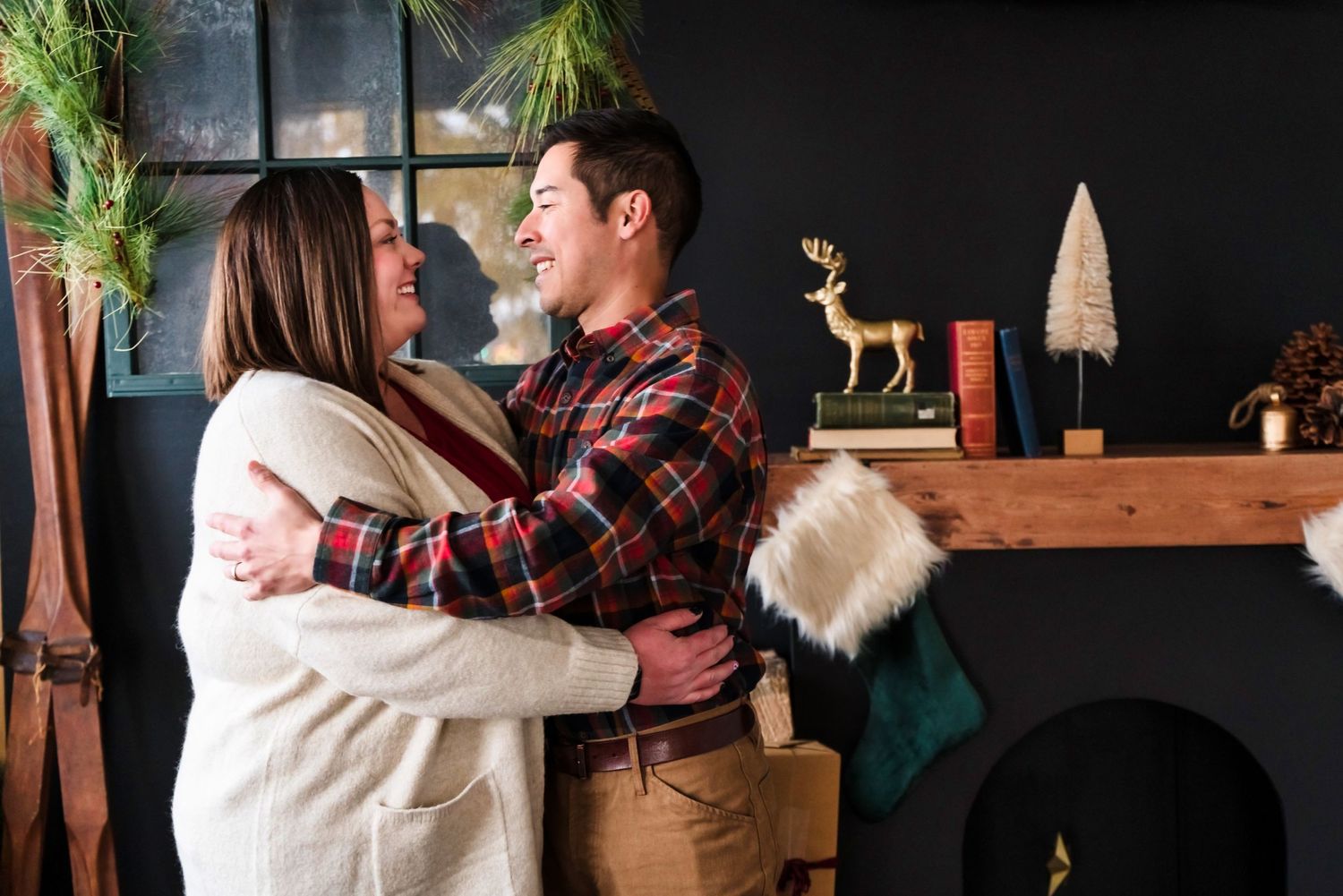 Couple embracing and laughing together near holiday decorations and wooden shelving.