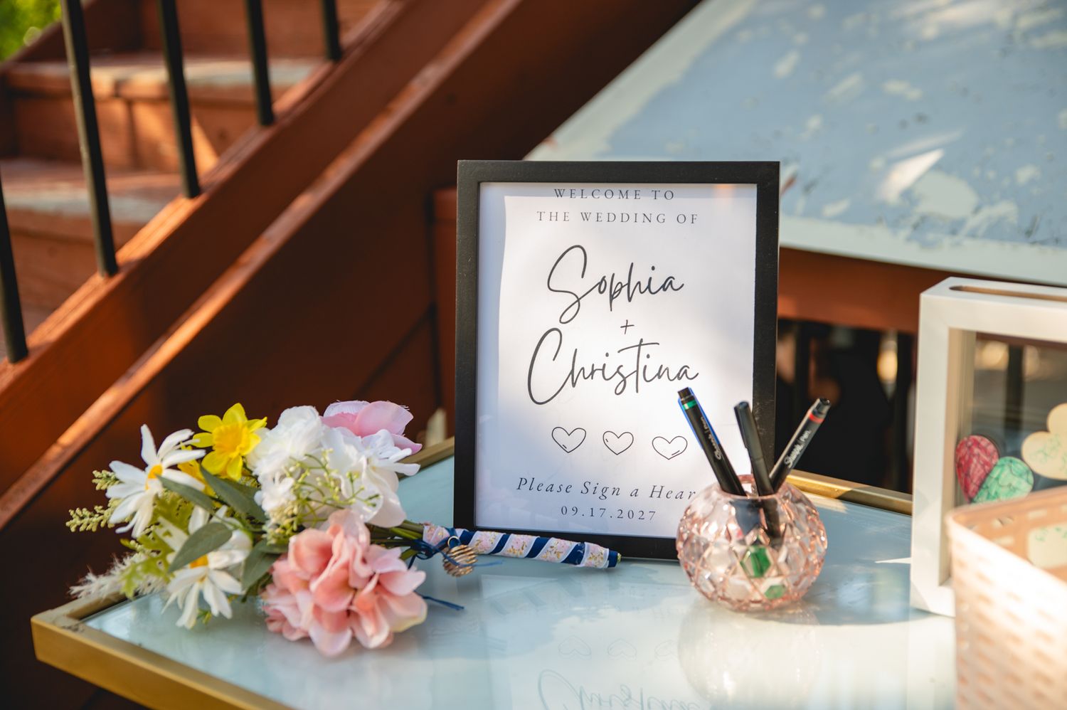 A wedding details table with a framed sign and pink and yellow flowers.