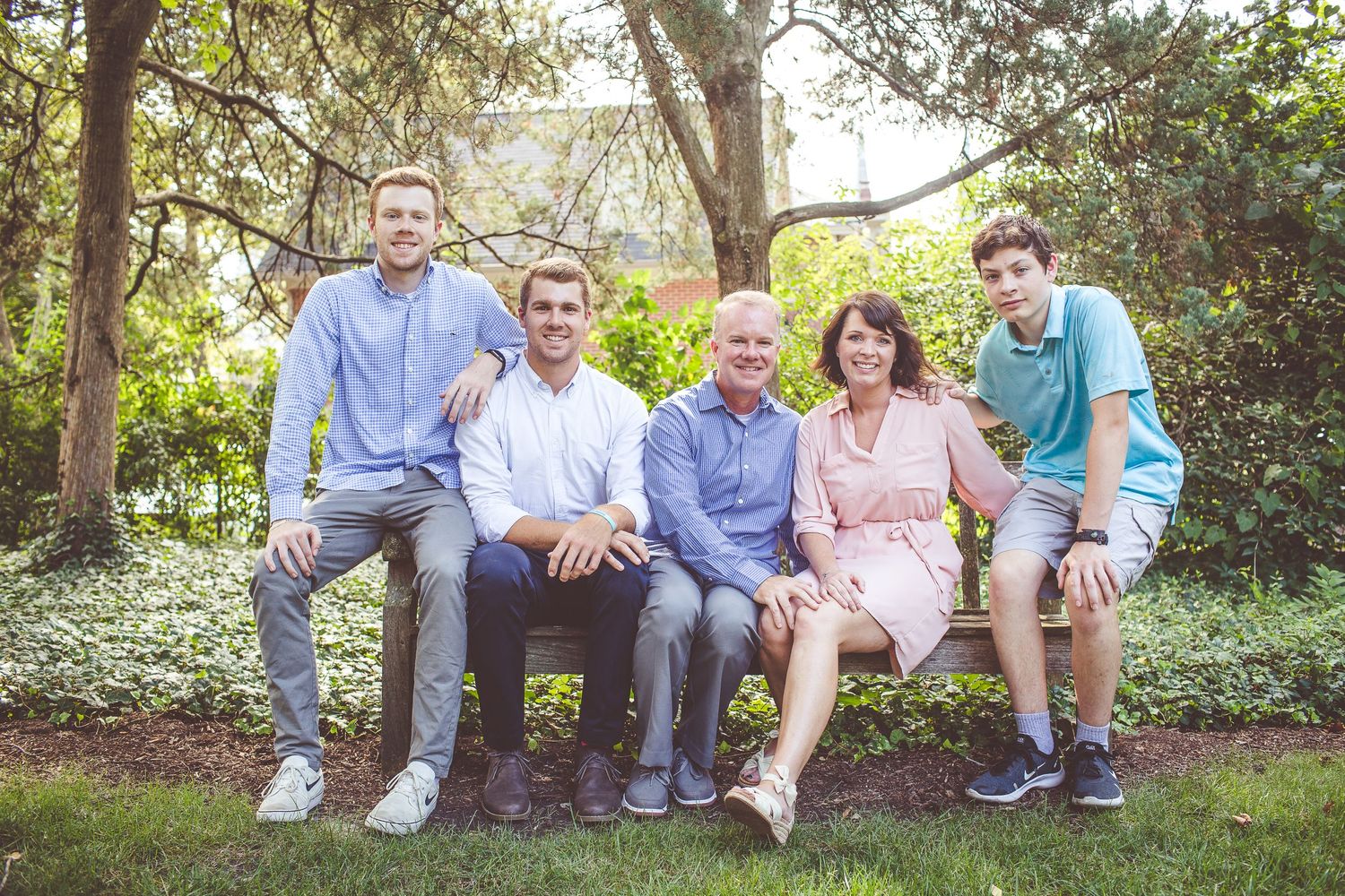 Family group poses together on wooden bench in lush garden setting.