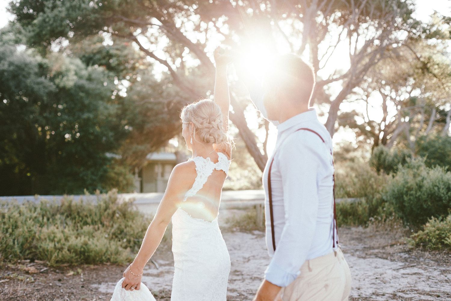 Sunlit silhouettes of newlyweds walking together along a beach path during golden hour.