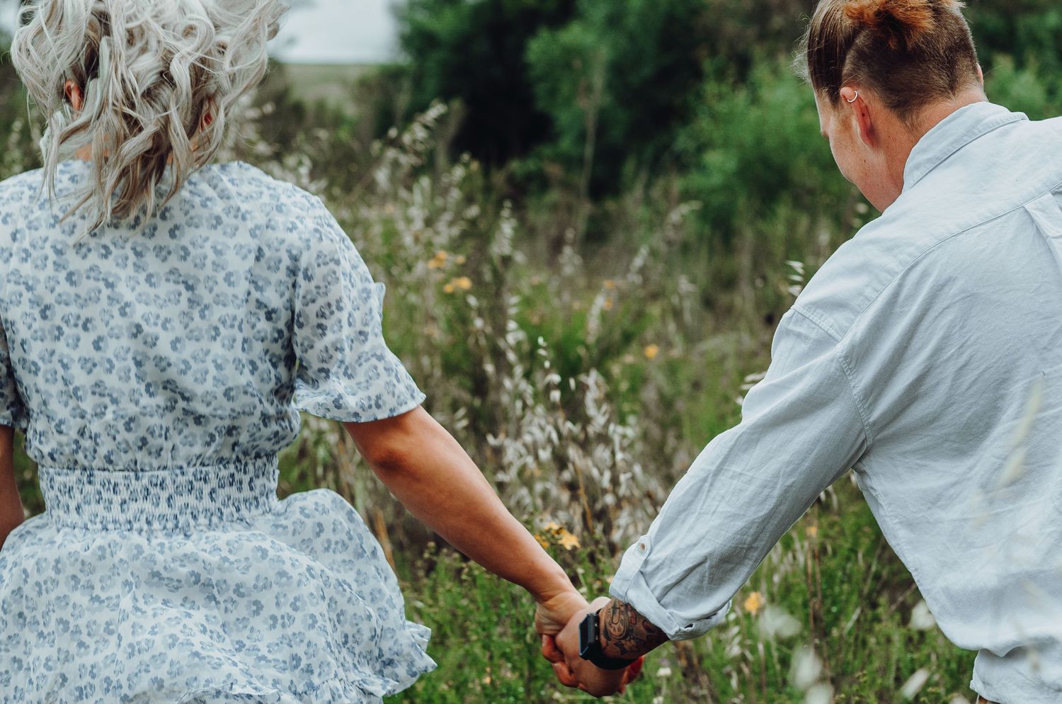 Couple holding hands while walking through wildflower meadow in summer.
