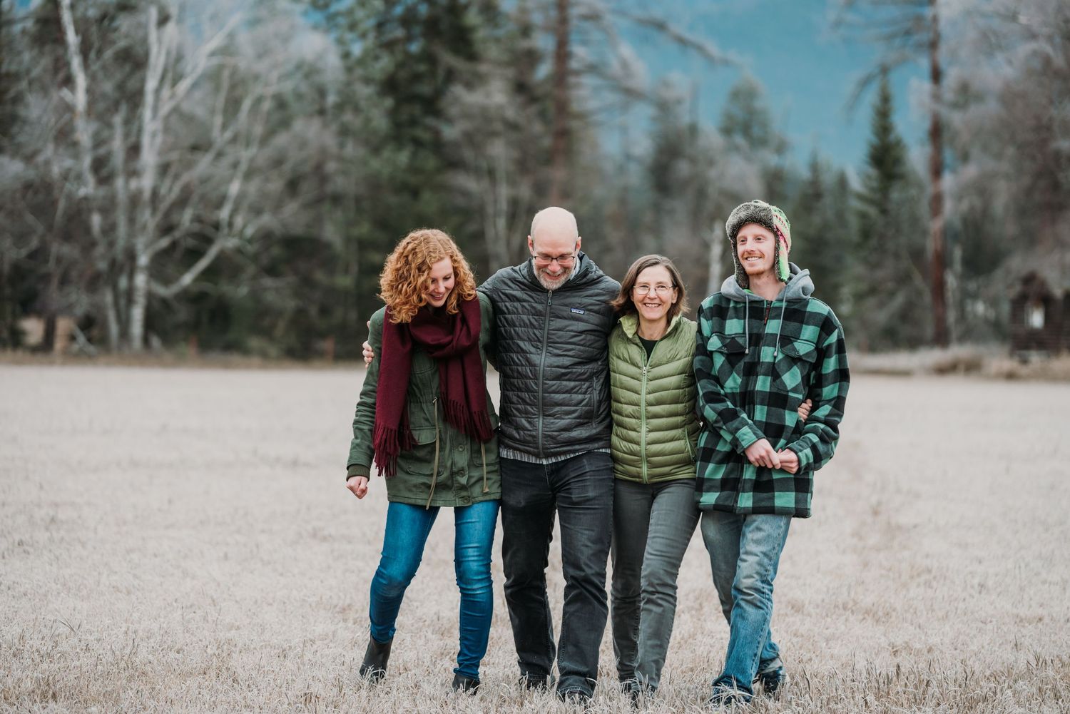 A group of people in winter clothing standing together on a gravel path surrounded by trees.