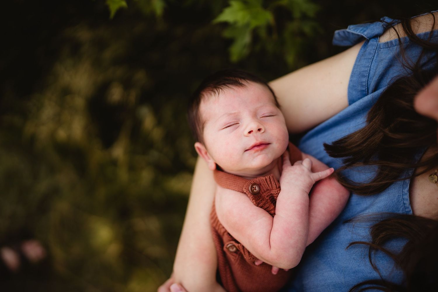 Newborn baby sleeping peacefully against blue fabric in natural outdoor setting.