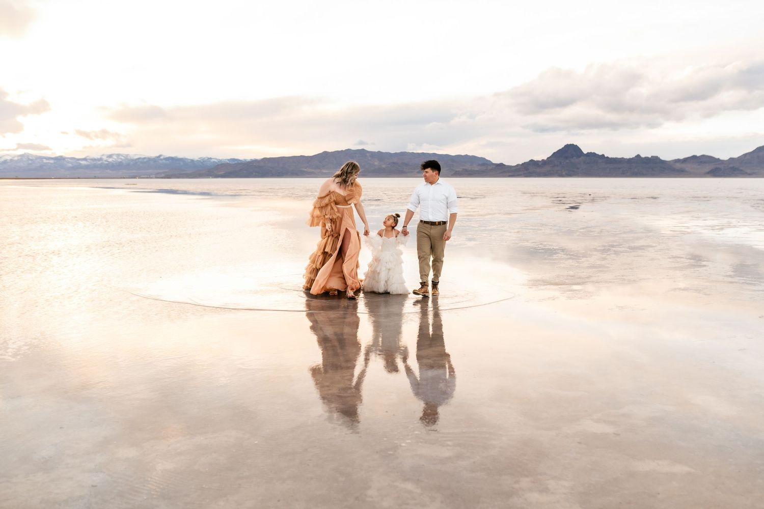 Family holding hands walking through the flooded Salt Flats together during golden hour.