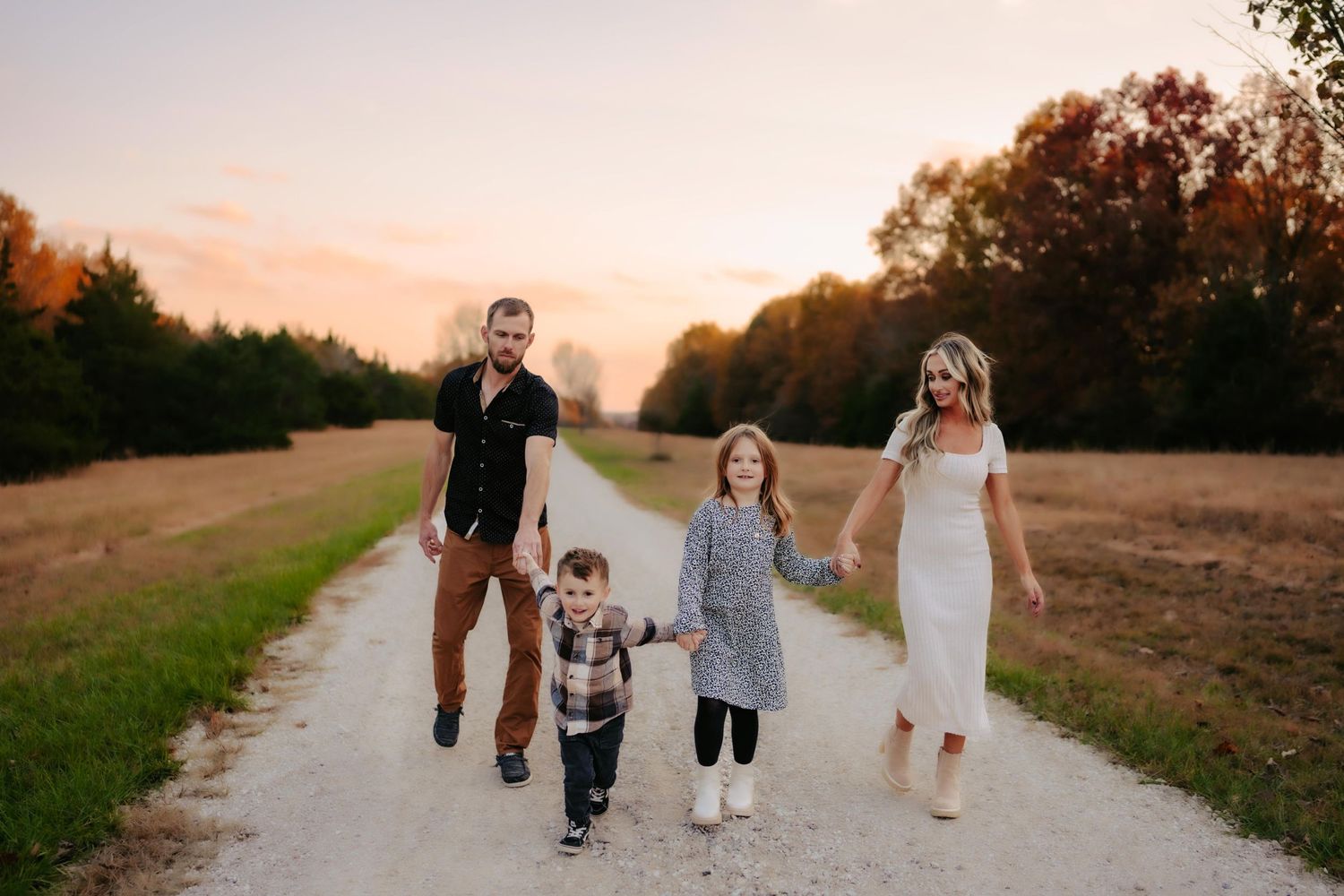 Happy family holding hands while walking together down a country road at sunset.