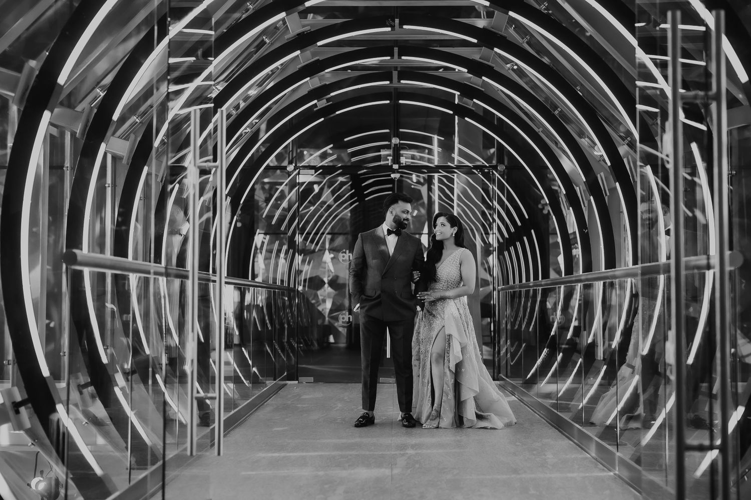 Black and white photo of a couple walking through a circular tunnel structure with dramatic lighting.