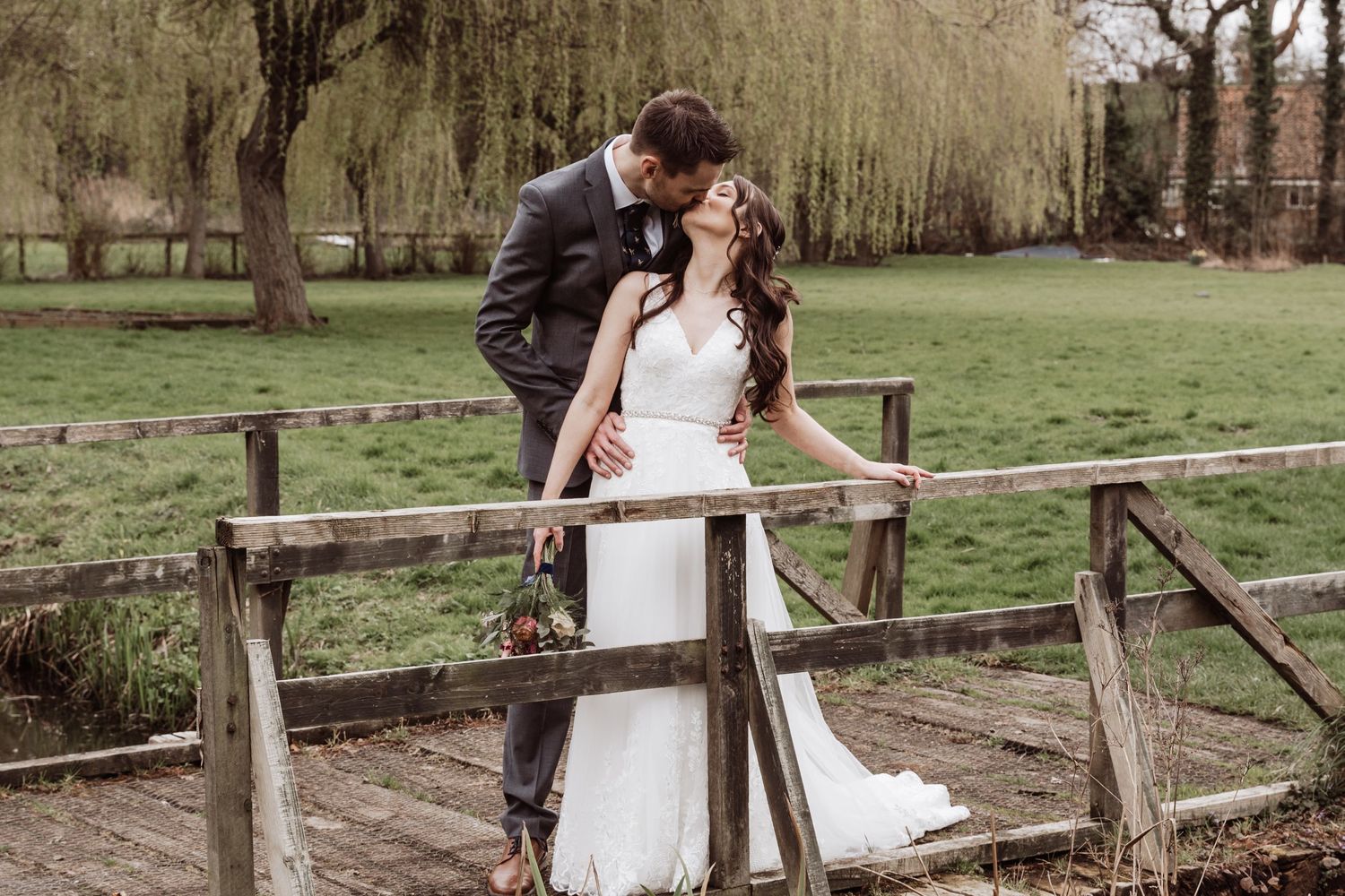 A bride and groom standing on a bridge kissing.