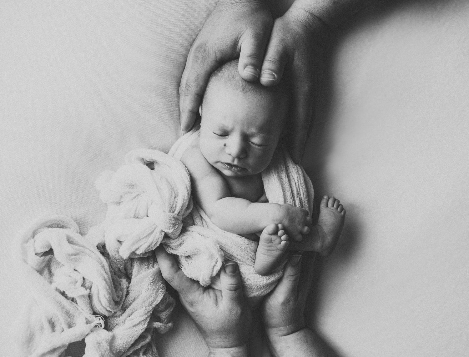 Black and white newborn photo of sleeping baby cradled gently in parents hands.