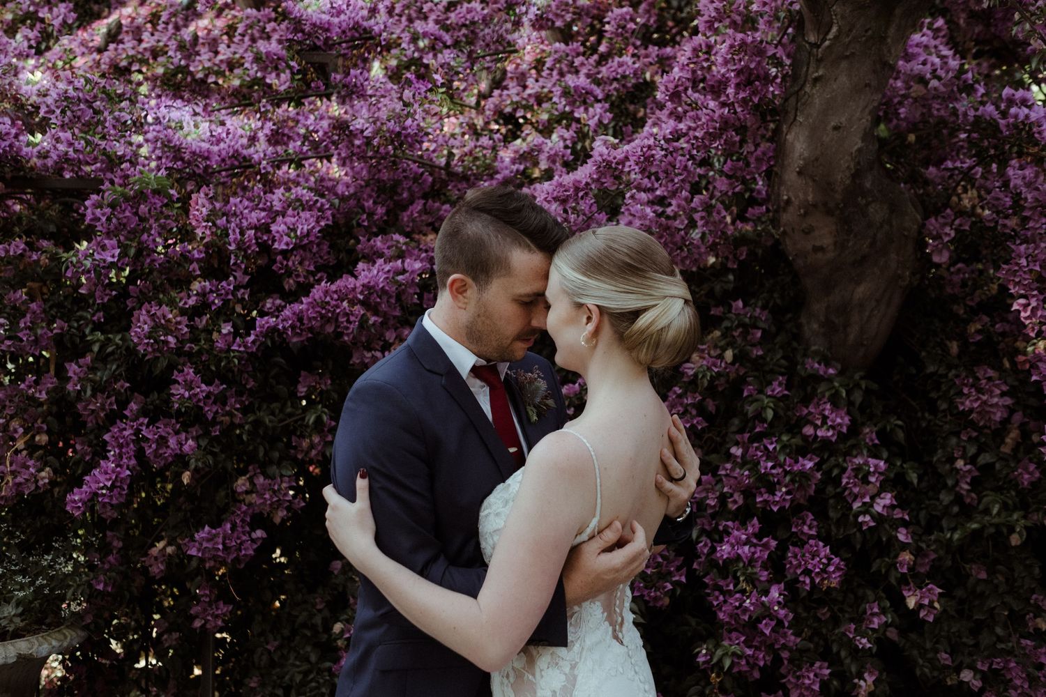 Bride and groom holding each other in front of bougainvilla flowers, Wouter Kleynhans Photography