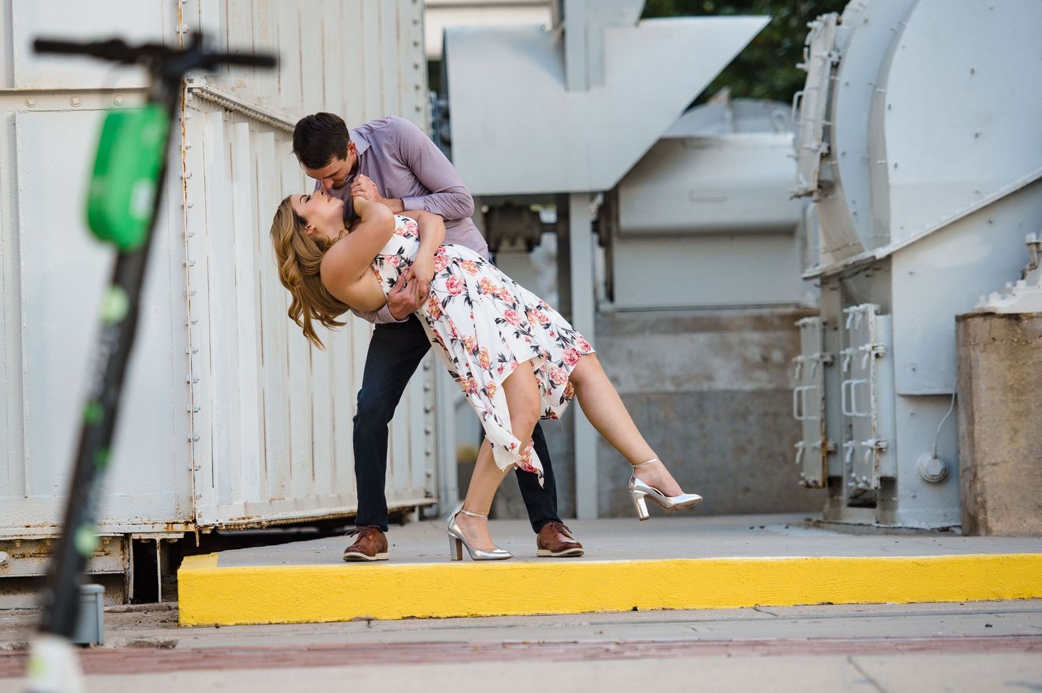A romantic dip pose captured in an urban setting with electric scooters visible.