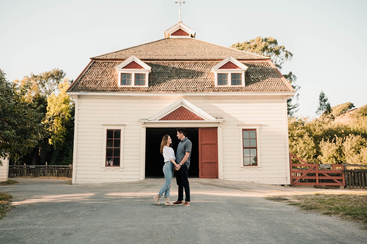 Couple poses in front of a white colonial style building with red door at dusk.