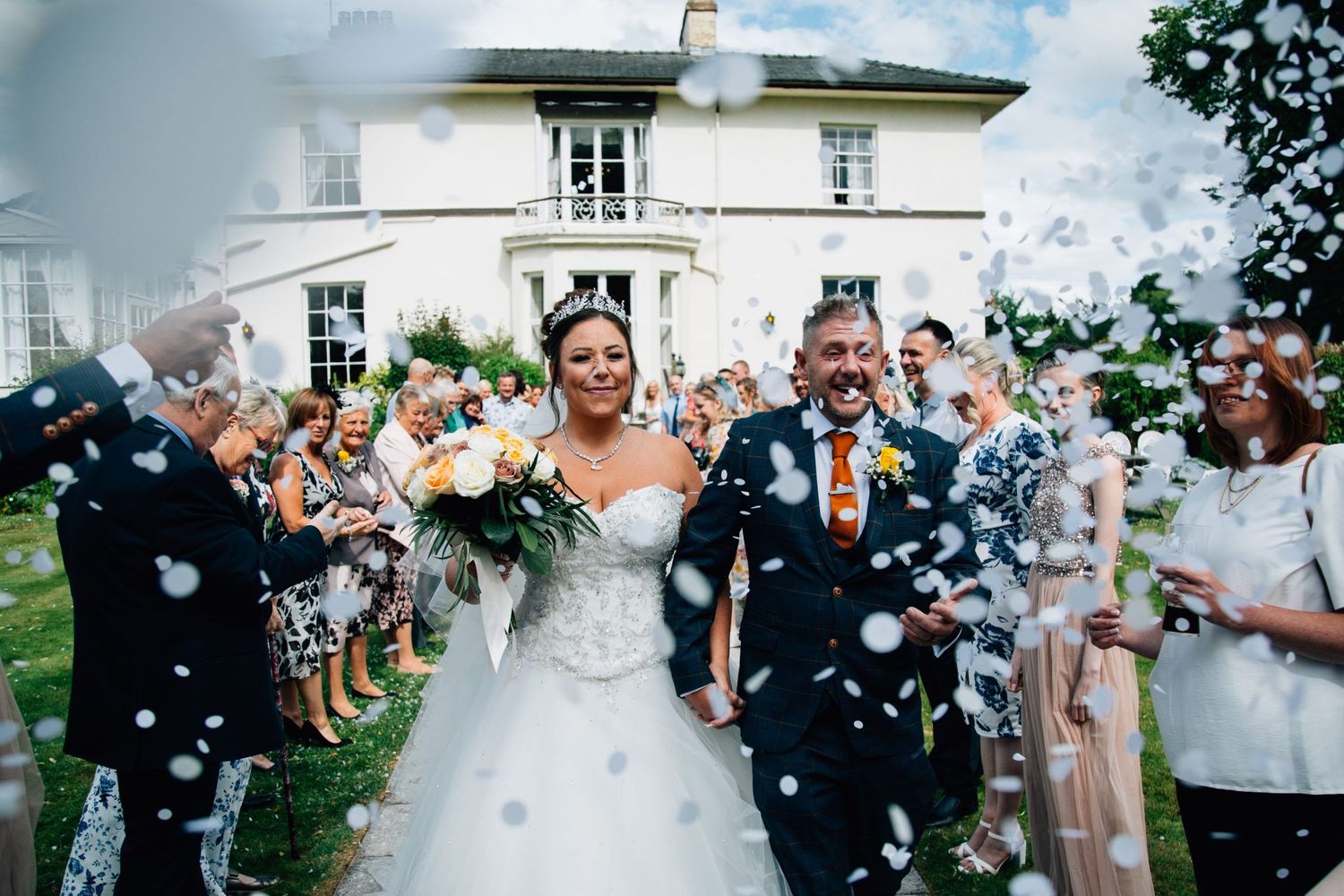 Wedding guests throwing confetti outside a grand building during a joyful celebration.