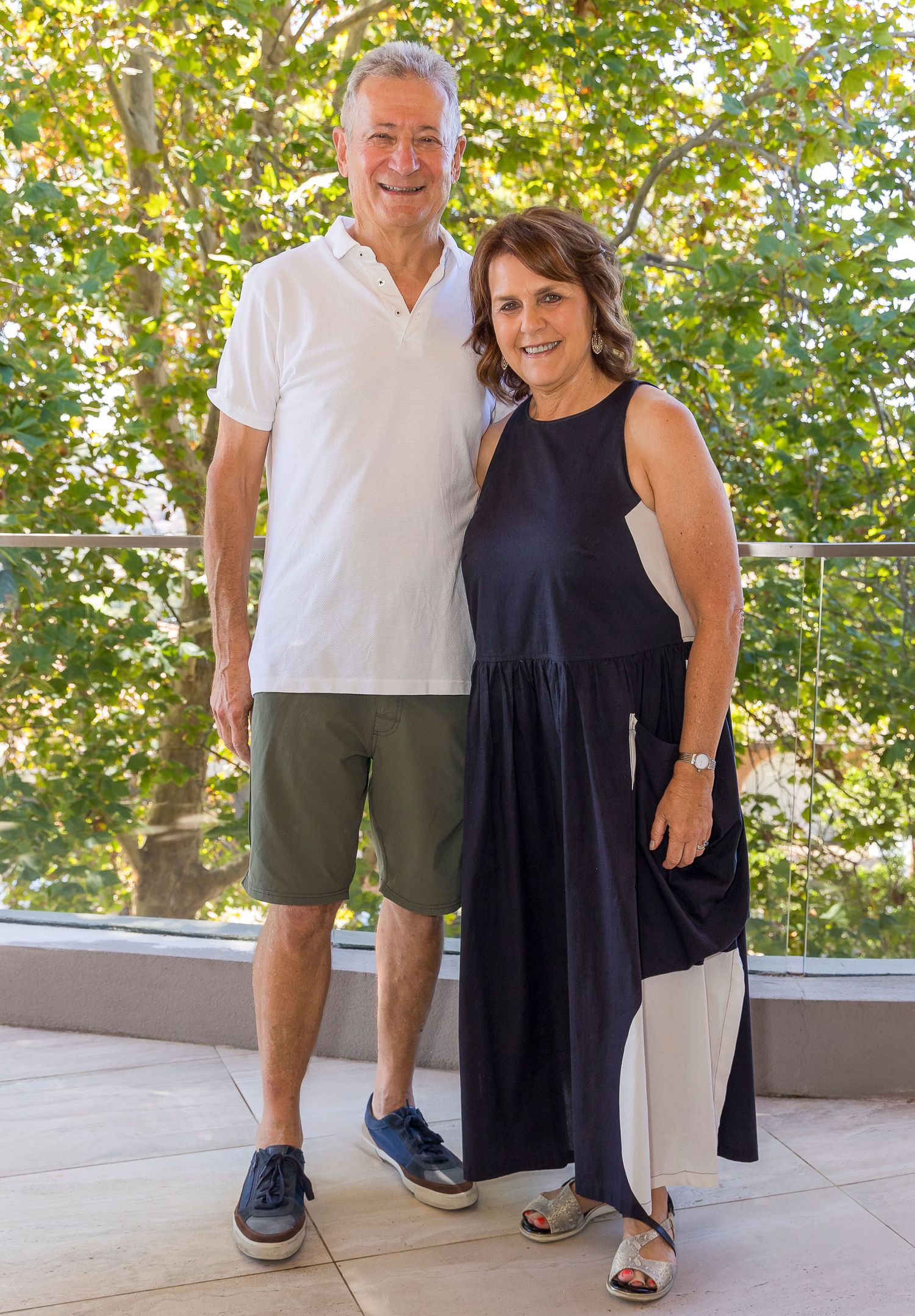 Couple posing on outdoor patio with white polo and navy dress in summer setting.