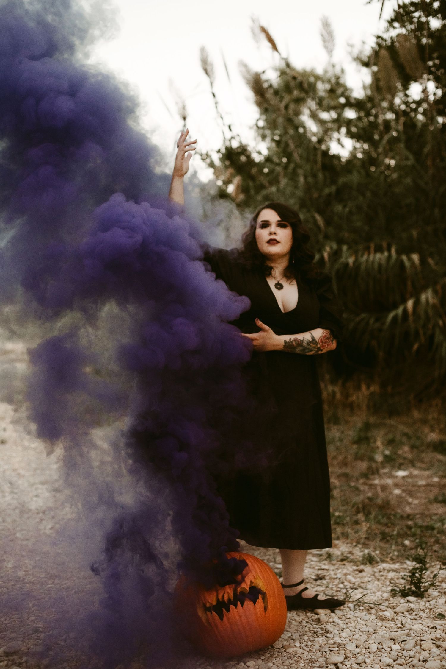 Halloween scene with purple smoke effect and carved pumpkin against natural backdrop.