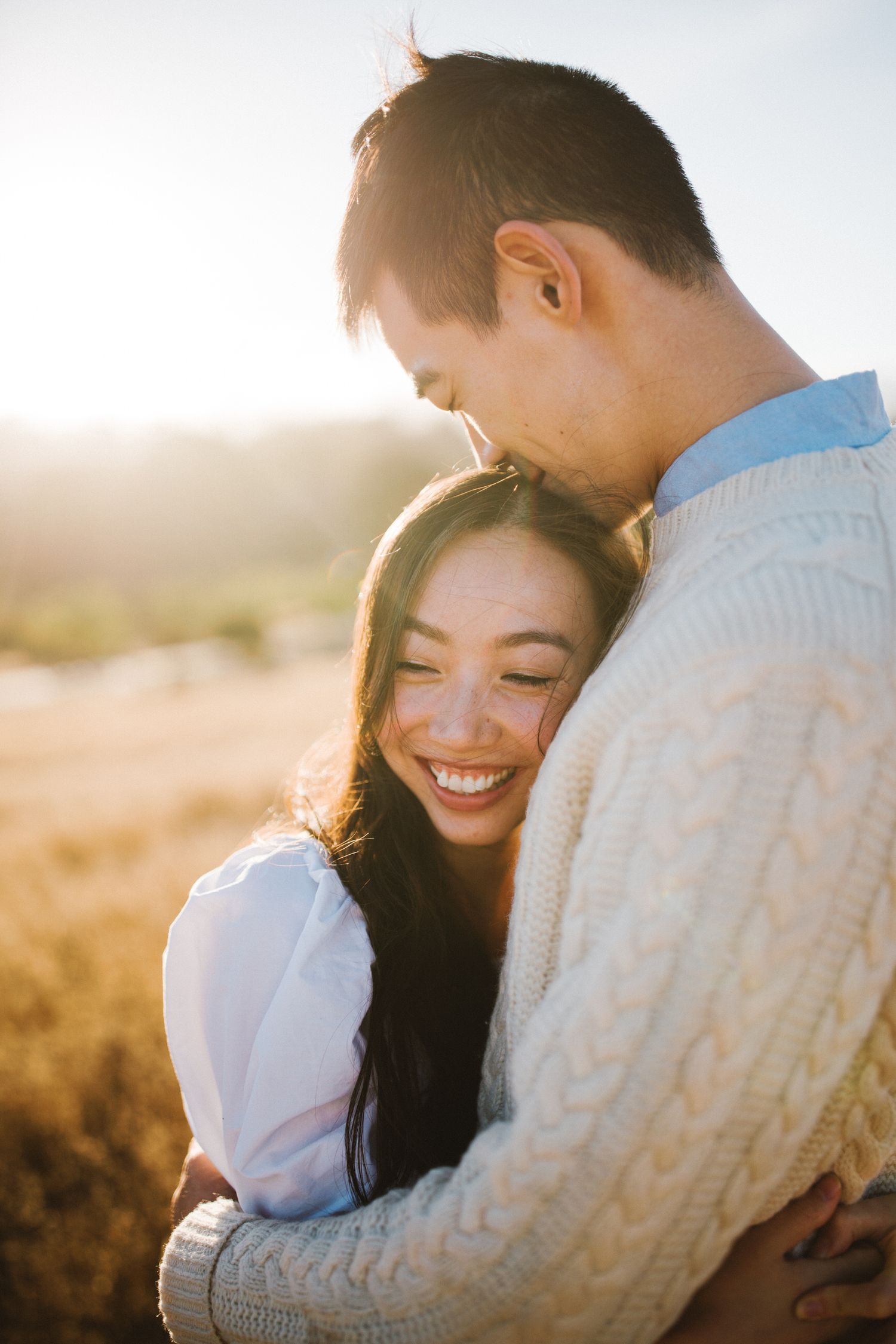 An intimate couple embraces in warm golden sunlight against a natural outdoor backdrop.