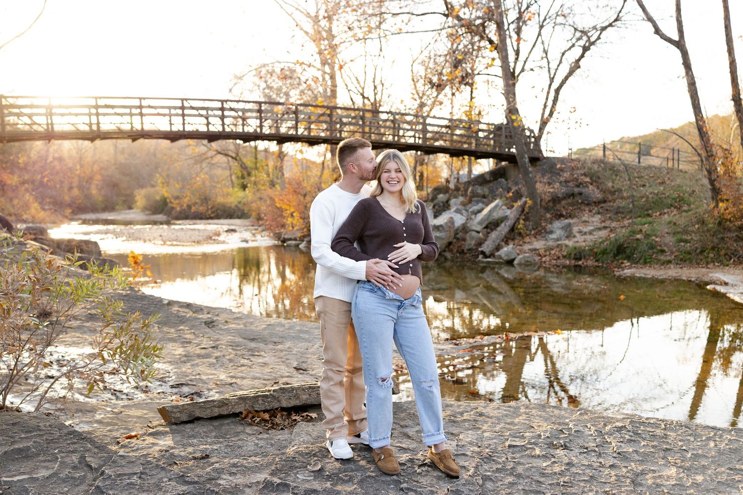 A group gathers at sunset near a rustic wooden bridge for outdoor portraits in a natural setting.