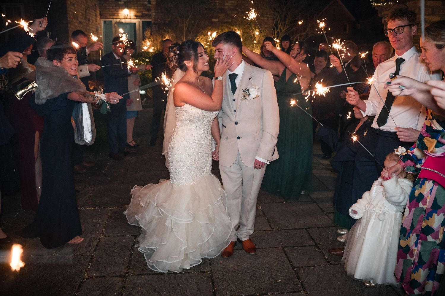 Wedding guests wave sparklers in celebration as a couple dances during an evening outdoor reception celebration.