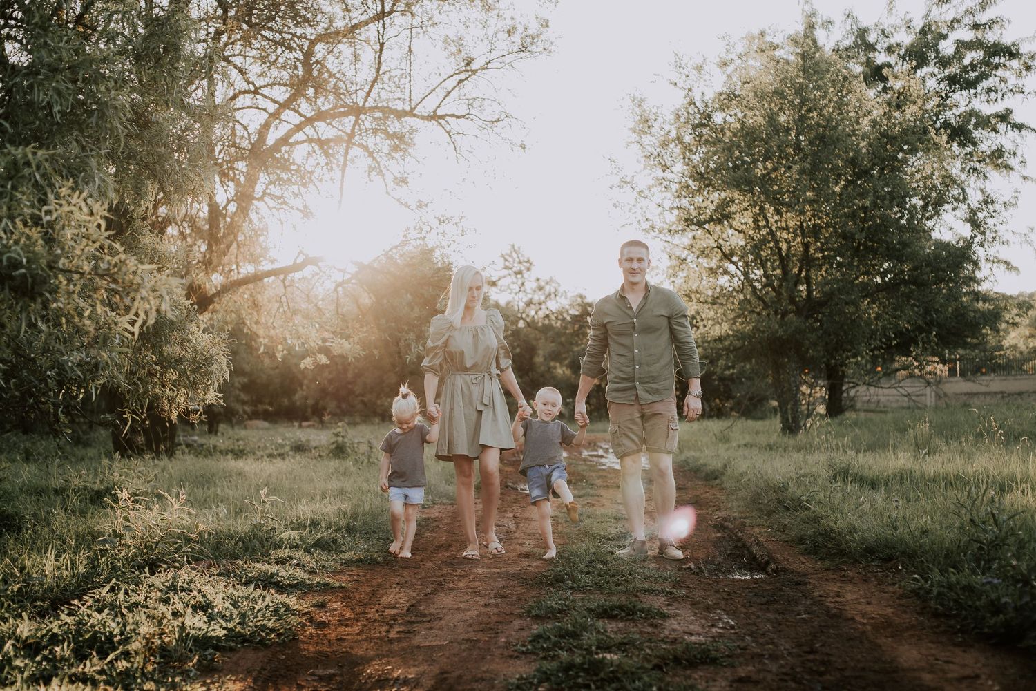 A group walks together on a dirt path through a sunlit field at golden hour with trees in the background.