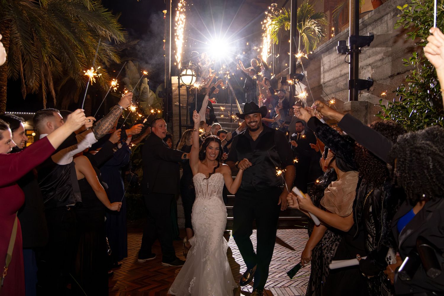Wedding guests hold sparklers in a dimly lit outdoor celebration creating a magical nighttime atmosphere.