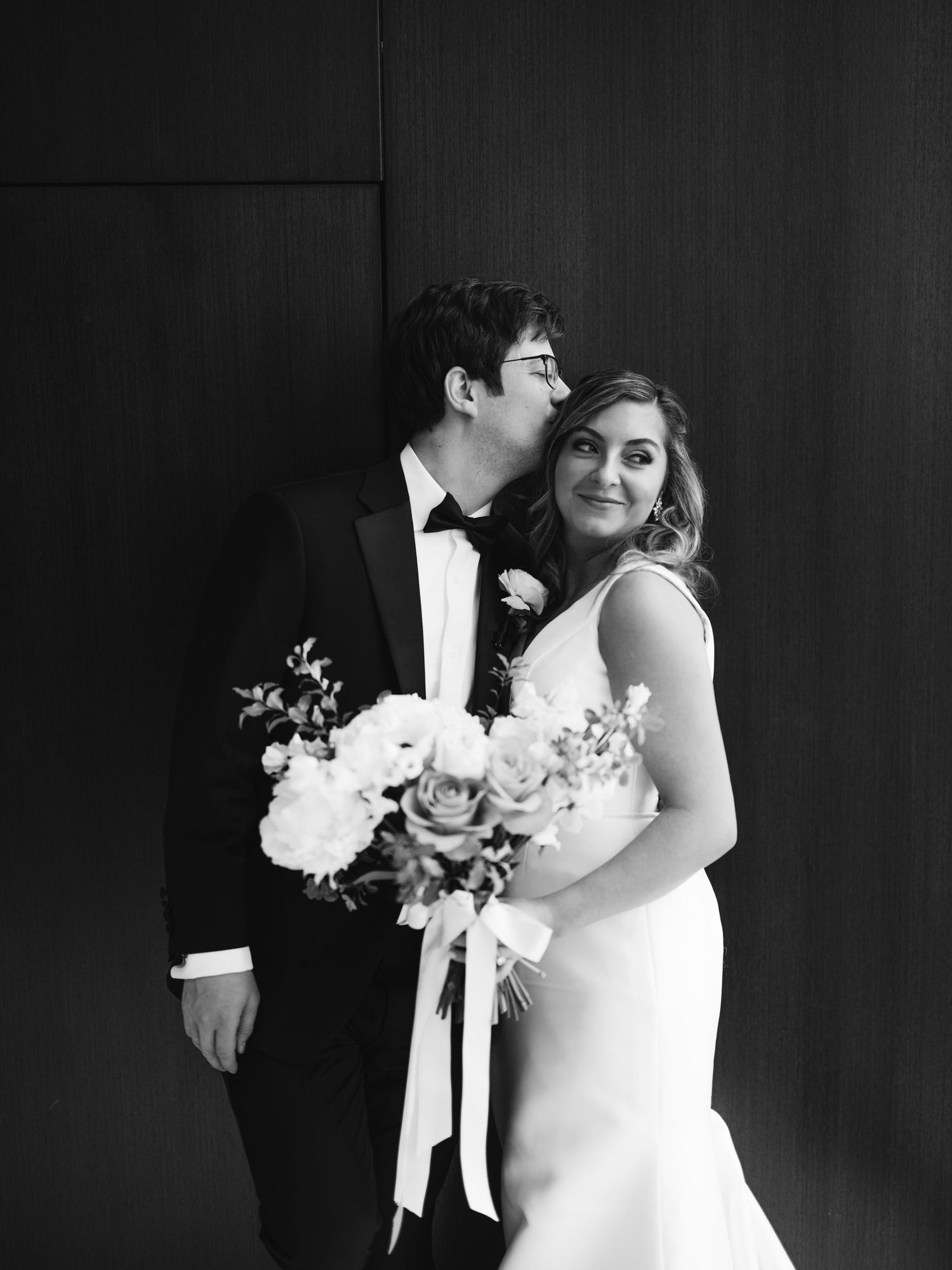 Black and white wedding photo showing a couple embracing with the bride holding an elegant floral bouquet.