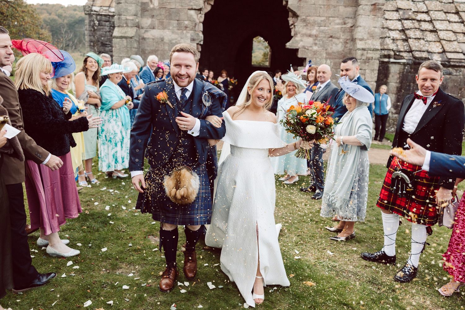 Joyful wedding celebration outside stone church with guests throwing confetti.