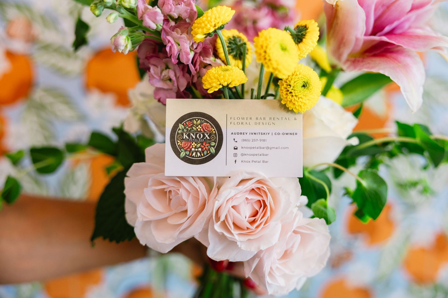 Vibrant floral arrangement featuring pink roses, yellow blooms and lilies with soft peach accents against a light background.